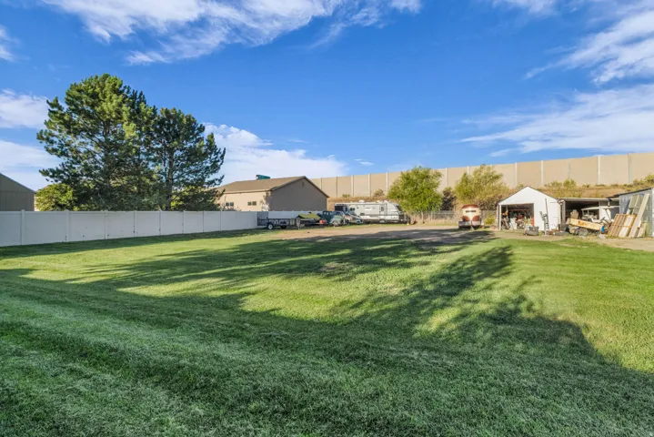 Expansive grassy area with a privacy fence, mature trees, and multiple outbuildings