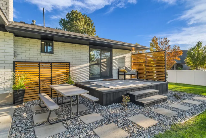 Exterior featuring a white brick facade, dark-toned decking with steps, and sliding glass door