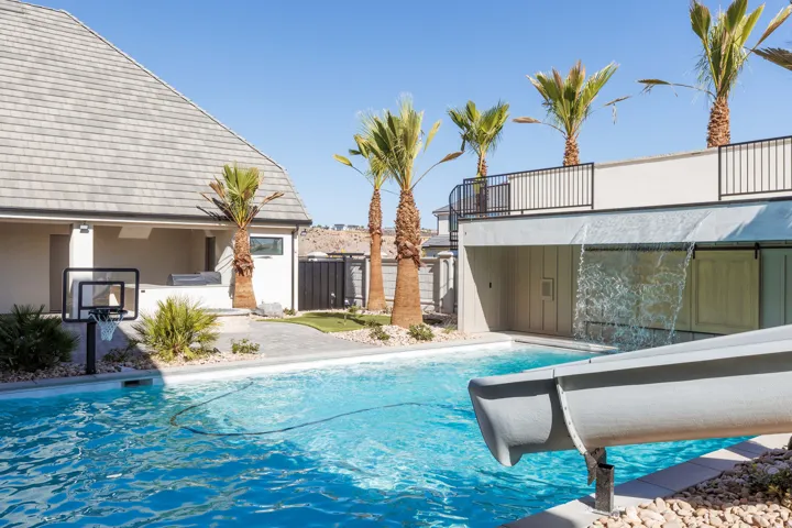 Expansive outdoor living area featuring a swimming pool, integrated water slide, cascading water feature, and a paved patio