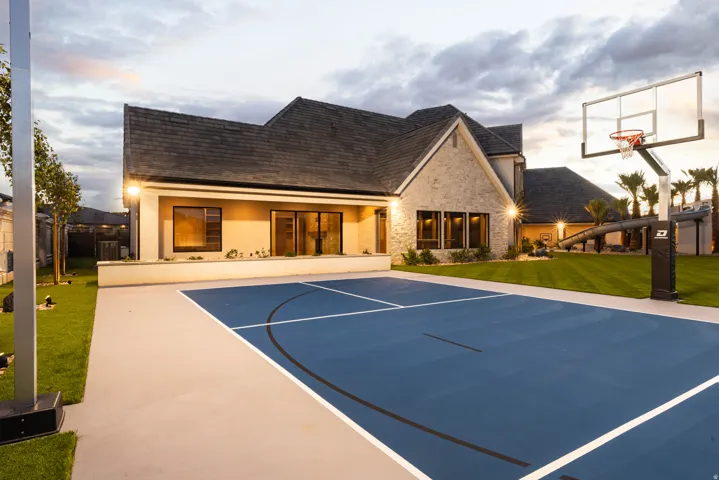Sport court with blue and gray surfacing, a basketball hoop, and surrounding manicured lawn