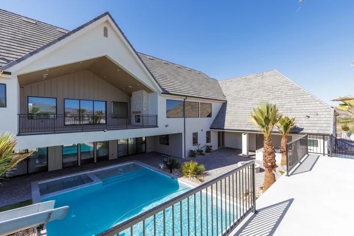 Exterior featuring a multistory design, a large in-ground pool with an integrated spa, an upper-level balcony with a fireplace, a lower-level patio, and extensive paved hardscaping