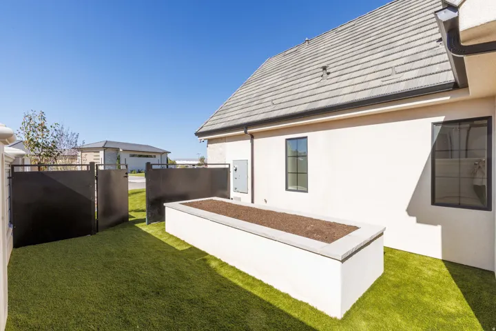 Stucco exterior with a tiled roof, featuring a built-in planter box, artificial turf, and dark-framed windows
