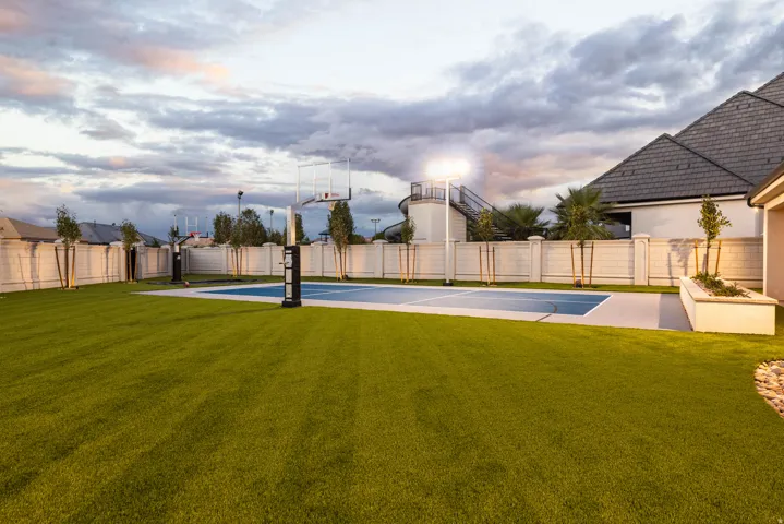 Expansive backyard featuring a manicured lawn, full-size sports court, and perimeter fencing