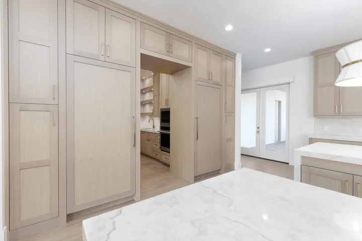 Integrated full-height refrigeration, extensive light wood-finish cabinetry, and a large central island with a stone countertop