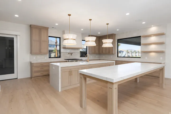 Expansive kitchen with wood-finish flooring, light wood cabinetry, stone countertops, and decorative pendant lighting