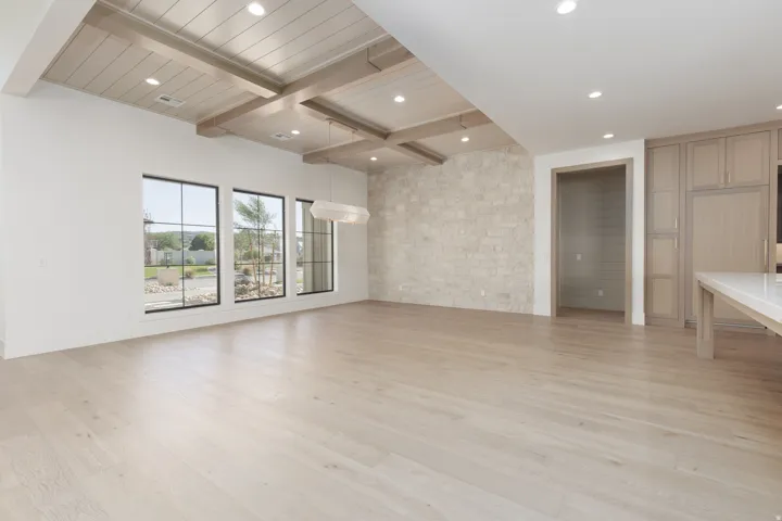 Wood-finish flooring with a stone accent wall, beamed ceiling, and recessed lighting
