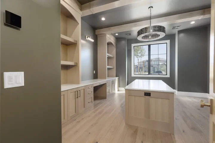 Built-in cabinetry with integrated desk, wood-finish flooring, central island with countertop, suspended chandelier, and large multi-pane window