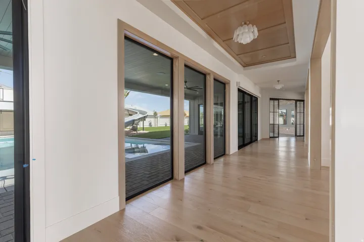 Light wood-finish flooring, recessed wood-paneled ceiling, modern semi-flush mount lighting, and large glass paneled doors