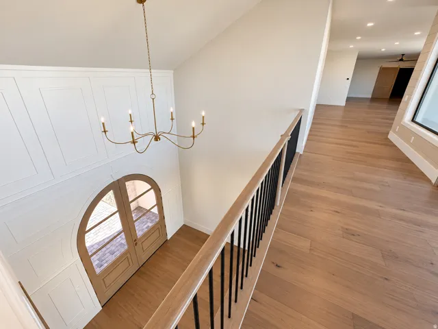 High ceilings with a brass chandelier, arched double entry doors, wainscoting detail, wood-finish flooring, and a staircase with a wood handrail and black balusters