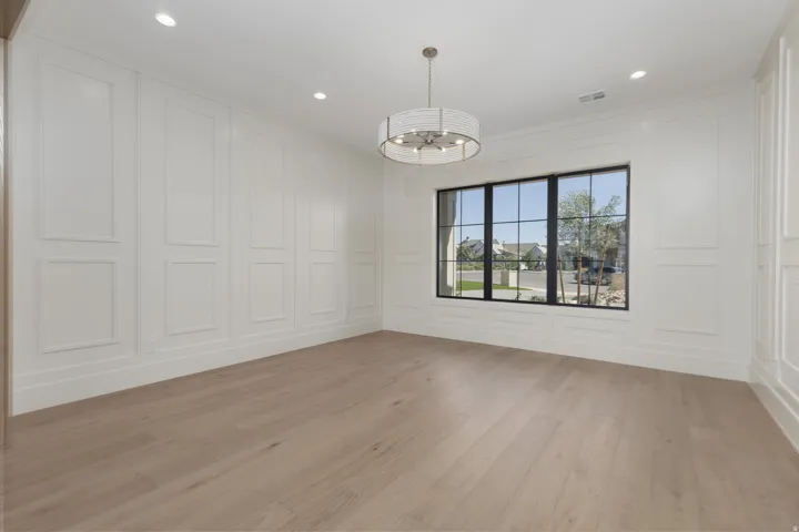 White panel molding, wood-finish flooring, recessed lighting, and a contemporary chandelier