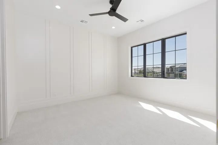 Panel molding accent wall, recessed lighting, black ceiling fan, large grid window, and light-colored carpeting