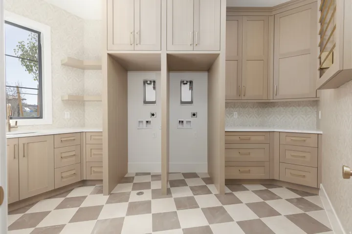 Custom cabinetry with ample storage, checkerboard floor tiles, white countertops, two appliance hookups, and a patterned wall finish