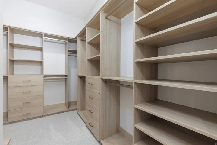 Custom closet system featuring light wood-finish shelving, multiple hanging rods, and integrated drawer storage