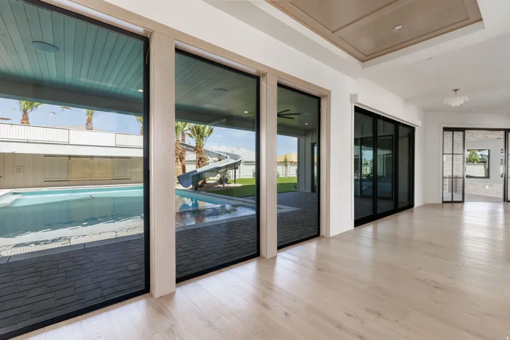 Light wood-finish flooring, coffered ceiling, multiple sets of glass panel sliding doors, and a decorative ceiling light fixture