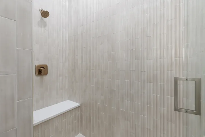 Shower featuring a fixed showerhead, coordinating control valve, built-in bench, recessed niche, and vertical tile with a textured finish