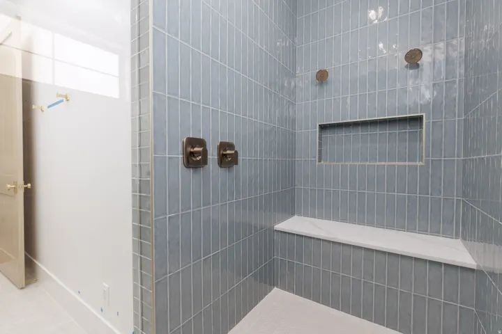 Shower featuring vertical blue-grey subway tile, a built-in niche, a white bench, and bronze-toned fixtures