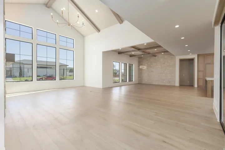 Vaulted ceiling with exposed beams, wood-finish flooring, floor-to-ceiling windows, stone accent wall, and built-in cabinetry