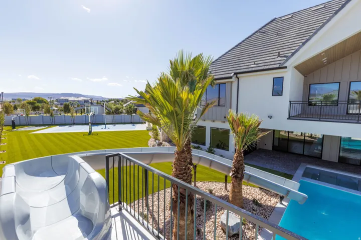 Expansive outdoor recreational area featuring a large grassy lawn, basketball court, swimming pool with water slide, and mature palm trees