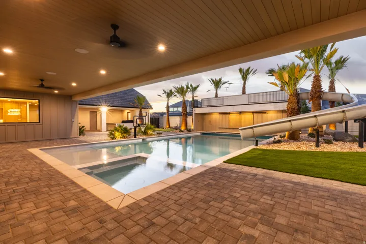 Paved patio with covered outdoor living space, integrated pool and spa, and a water slide