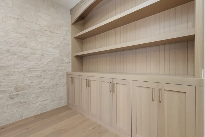Built-in cabinetry with flat panel doors, integrated shelving with beadboard backing, stone veneer wall, and wood-finish flooring