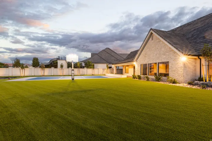 Expansive green lawn with a dedicated sports court, stone exterior, and dark-pitched roof
