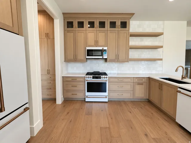 Kitchen featuring wood-finish flooring, light wood cabinetry, a tile backsplash, white countertops, and a white range