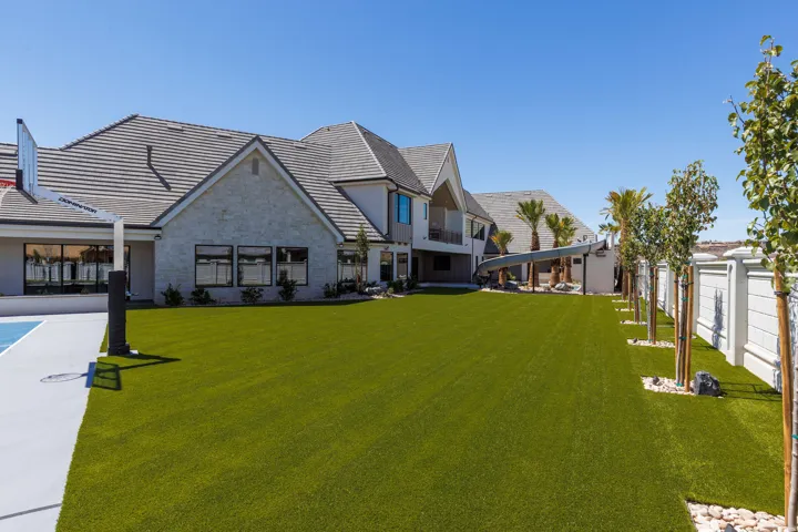 Expansive green space, paved sports court with basketball hoop, mature trees, stone-clad exterior, and a covered outdoor structure