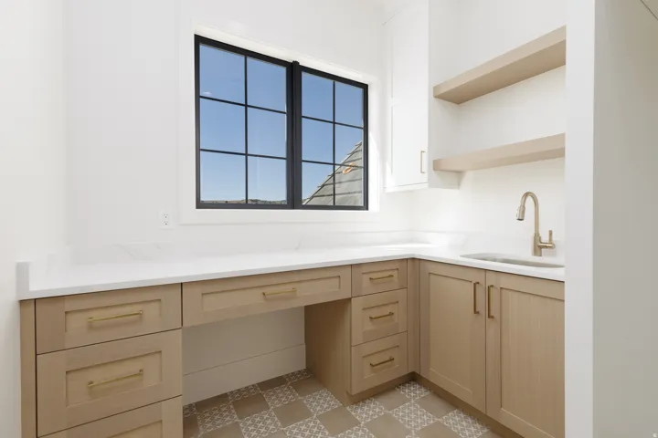 Built-in desk area with light wood-finish cabinetry, white countertop, and patterned floor tiling