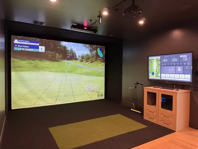 Dedicated golf simulator room featuring a large projection screen, wall-mounted display, recessed lighting, and track lighting