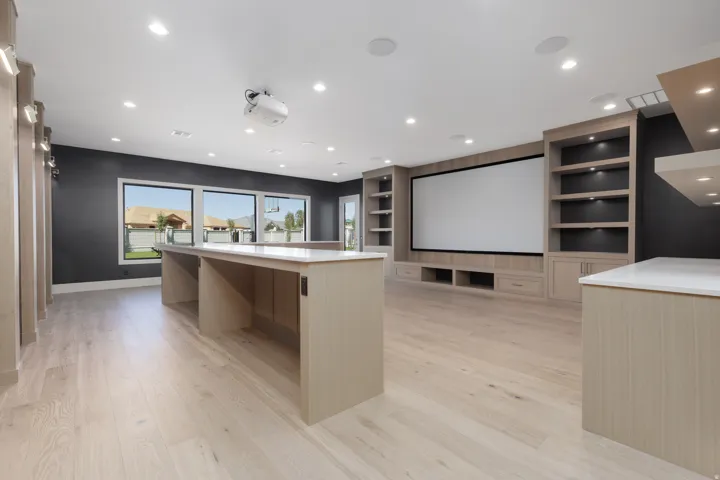 Large entertainment room featuring light wood-finish flooring, built-in shelving, a large projection screen, and integrated recessed lighting
