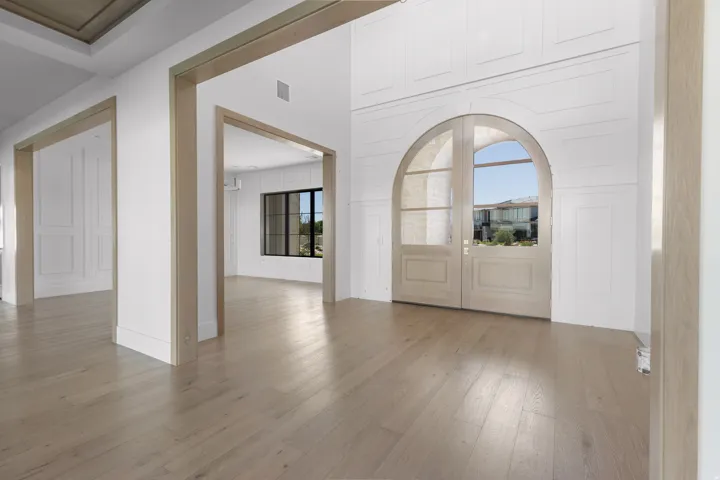 Wide plank wood-finish flooring, arched double entry doors, wood paneling, and wood-trimmed doorways