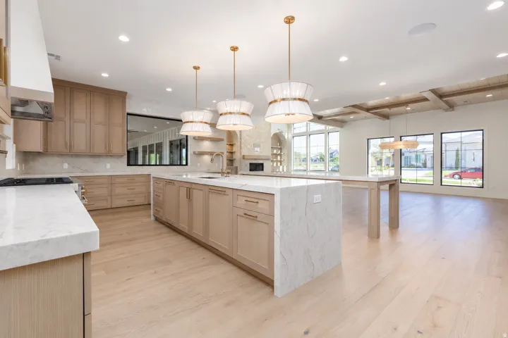Open-concept kitchen and living area featuring light wood-finish flooring, a large kitchen island with a stone countertop, and custom cabinetry