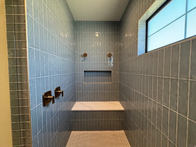 Tiled shower with a built-in bench, recessed niche, window, and bronze-finish fixtures