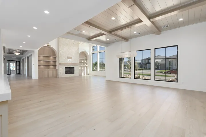 Spacious living area featuring light wood-finish flooring, a stone-clad fireplace with a hearth, and dual arched built-in shelving units with integrated lighting