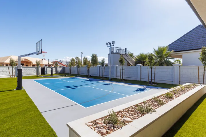 Outdoor court with blue surfacing, surrounded by artificial turf and a perimeter wall