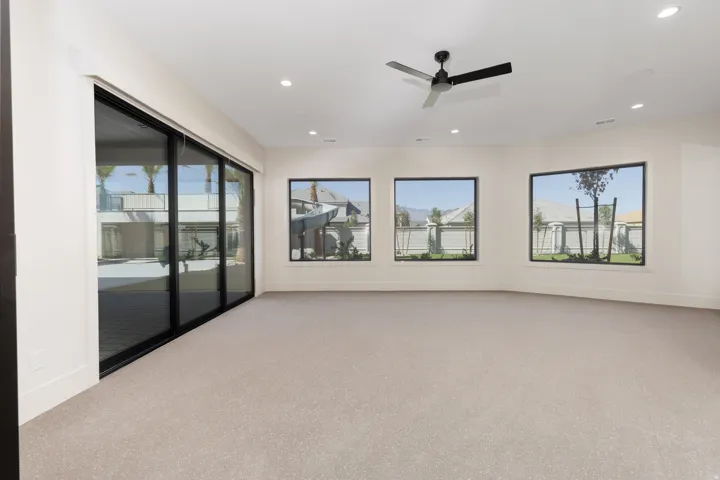 Expansive carpeted room featuring a large sliding glass door, three picture windows, a ceiling fan, and recessed lighting