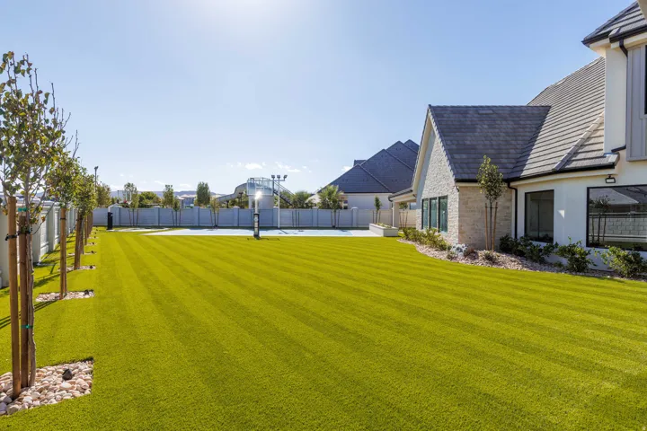 Expansive artificial turf lawn with a sport court, mature trees, and landscaping