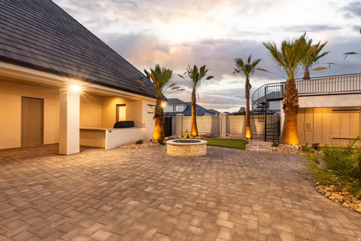 Paver courtyard featuring a built-in outdoor kitchen, stone-finish fire pit, artificial turf putting green, and mature palm trees