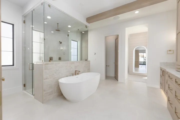 Freestanding soaking tub, glass-enclosed shower with tile surround, dual vanities with stone countertops, and light wood-finish cabinetry