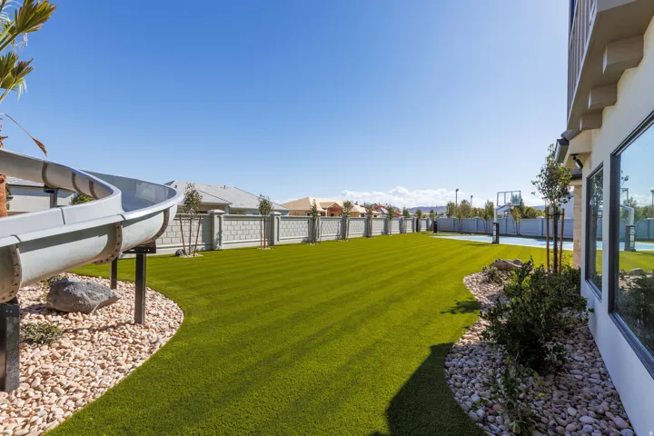 Expansive backyard featuring a manicured lawn, built-in water slide, decorative rock landscaping, and a fenced sports court