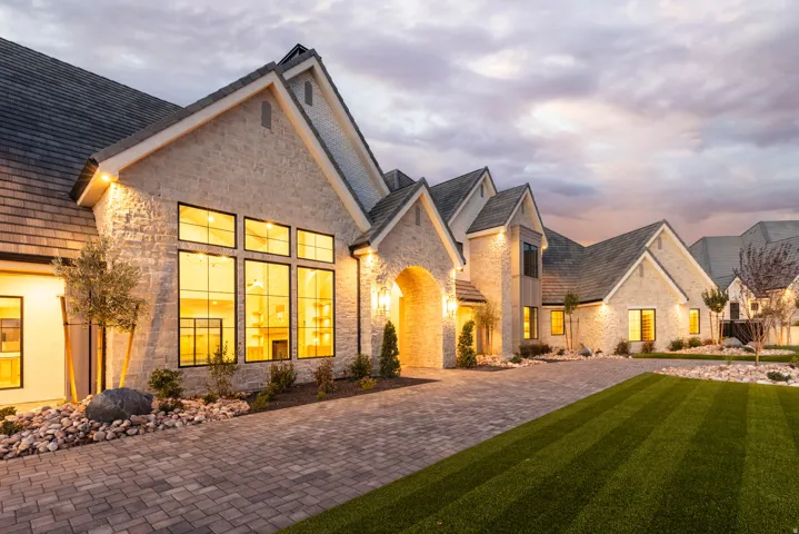 Stone facade home featuring multiple gables, an arched entry, a paver driveway, and manicured landscaping with a rock garden