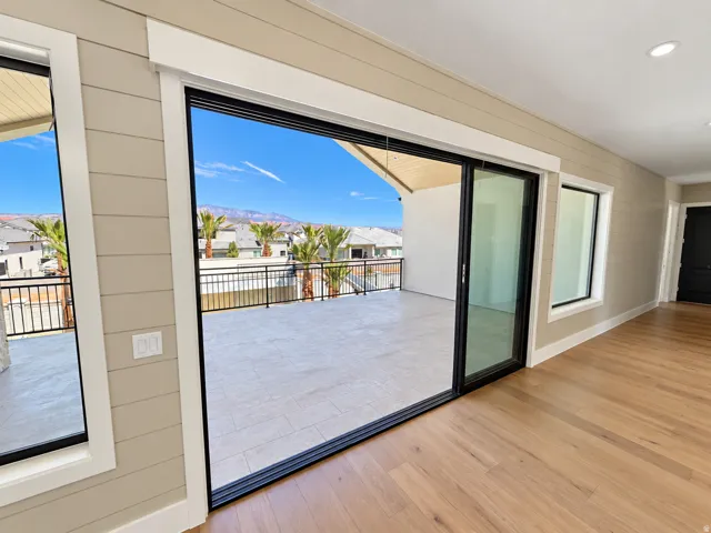 Expansive outdoor patio with tile flooring and black metal railing, large sliding glass doors, light wood-finish flooring, and horizontal plank wall paneling
