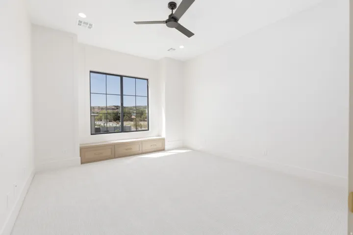 White wall finish, black ceiling fan, recessed lighting, large window with black grid, built-in window bench with storage, white carpet flooring