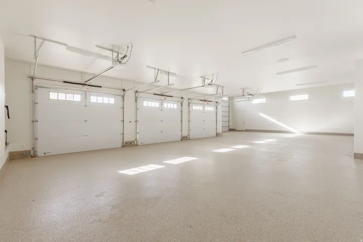 Three overhead garage doors with window accents, light-toned epoxy flooring, multiple fluorescent light fixtures, and high-set windows