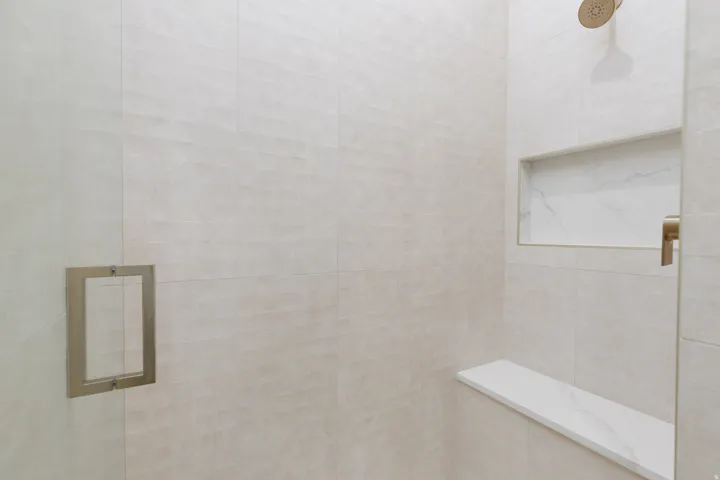 Shower enclosure featuring large format wall tiles, a built-in shower niche, a shower bench, and a brushed brass shower head and handle