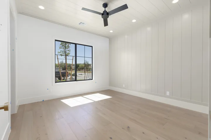 Wood-finish flooring, accent wall with vertical paneling, recessed lighting, ceiling fan, and a black-framed window