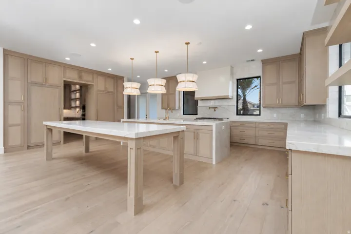 Gourmet kitchen with light wood-finish cabinetry, two large islands with stone countertops, integrated appliances, and wood-finish flooring