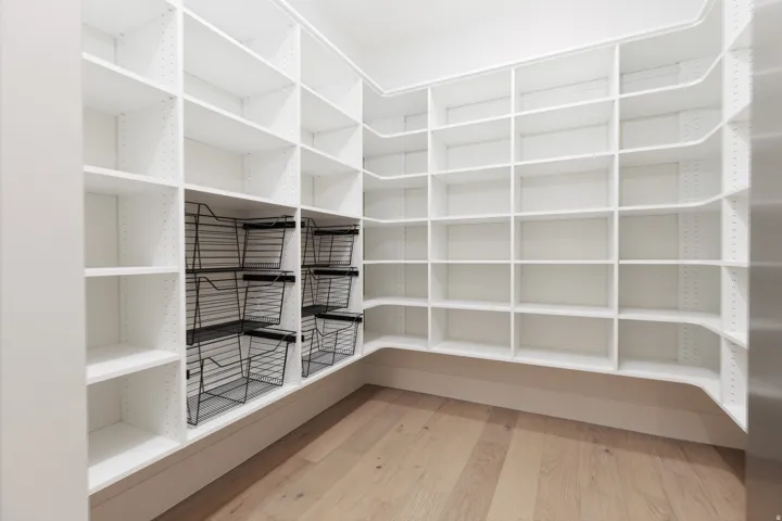 Custom built-in shelving with adjustable white shelves, integrated wire baskets, and wood-finish flooring