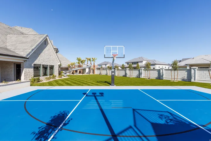 Spacious backyard featuring a full-sized basketball court, manicured lawn, and a stone-clad exterior