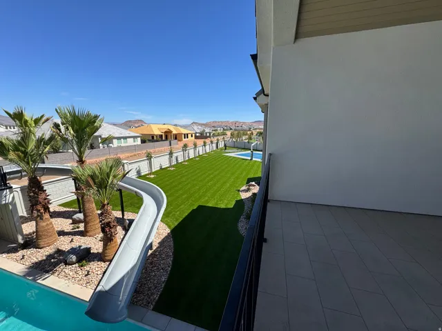 Landscaped backyard with a swimming pool, a waterslide, and synthetic turf